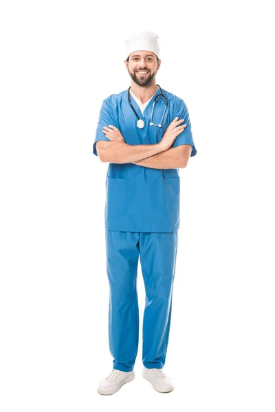 Full length view of bearded surgeon standing with crossed arms and smiling at camera isolated on white — Stock Photo