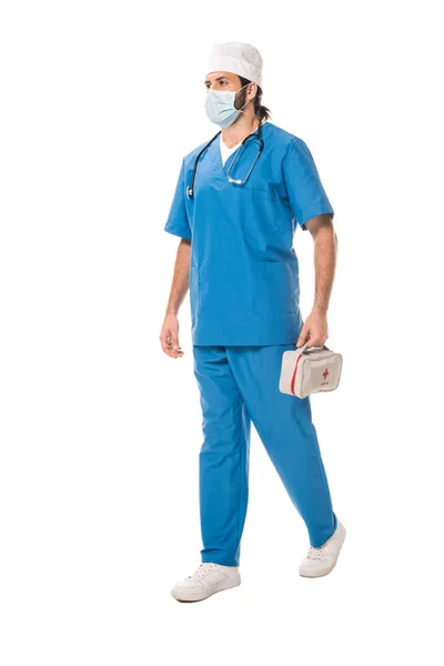 Vista completa del medico in maschera medica che tiene kit di pronto soccorso e cammina isolato su bianco — Foto stock
