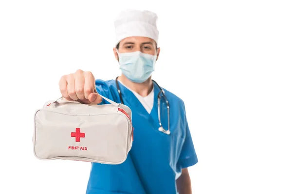 Vista de cerca del médico en máscara médica que sostiene el botiquín de primeros auxilios aislado en blanco - foto de stock