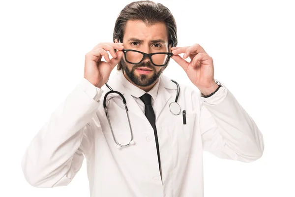 Doctor barbudo en bata blanca ajustando gafas y mirando a la cámara aislada en blanco - foto de stock