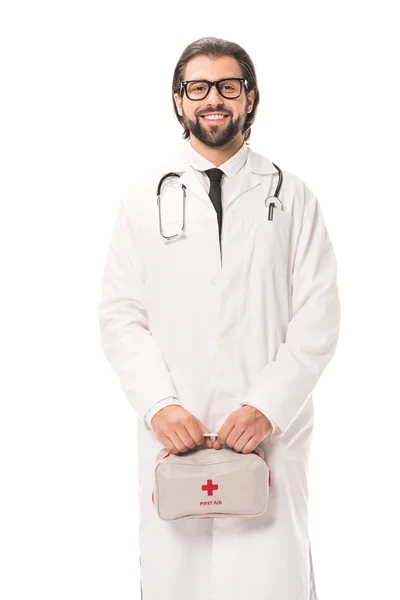 Doctor en anteojos sosteniendo botiquín de primeros auxilios y sonriendo a cámara aislada en blanco - foto de stock