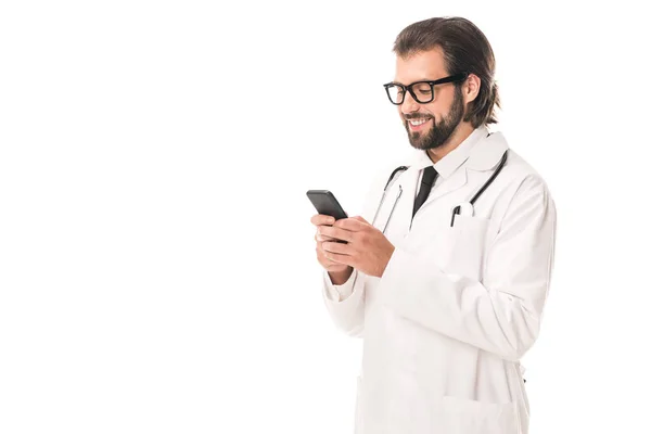 Médecin souriant dans des lunettes et manteau blanc en utilisant smartphone isolé sur blanc — Photo de stock