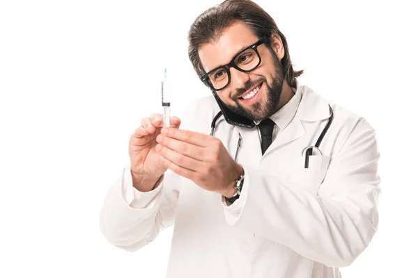 Happy doctor holding syringe and talking by smartphone isolated on white — Stock Photo