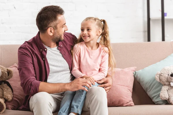 Fille souriante assise sur les genoux du père sur le canapé — Photo de stock