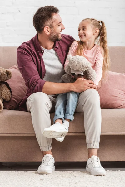 Hija sosteniendo osito de peluche de rodillas padre y mirándose el uno al otro - foto de stock