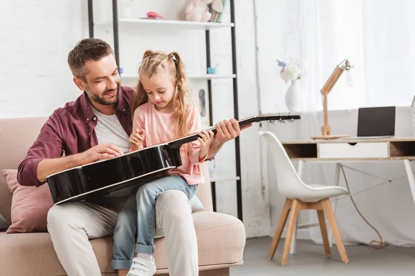 Padre e hija divirtiéndose y tocando la guitarra en el sofá - foto de stock