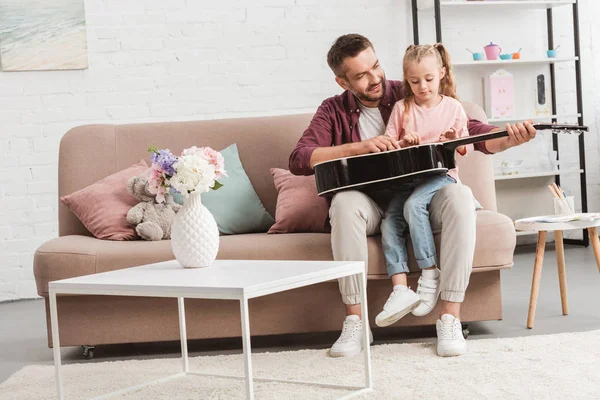 Padre e hija divirtiéndose y tocando la guitarra en el sofá - foto de stock