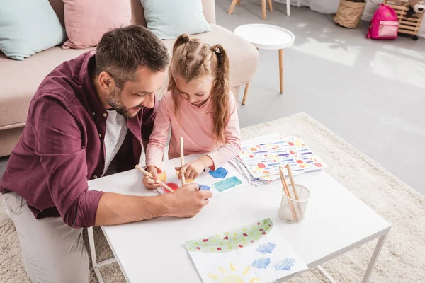 Padre e hija se divierten y dibujan en la mesa blanca - foto de stock