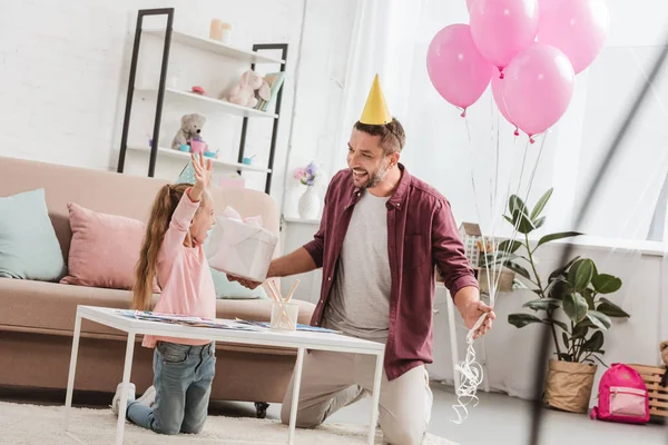 Padre con globos rosados y regalo divirtiéndose con hija - foto de stock
