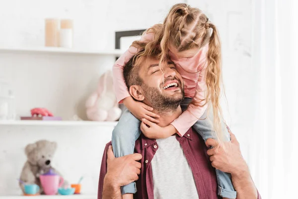 Hija sentada sobre los hombros de los padres y abrazándose en casa - foto de stock