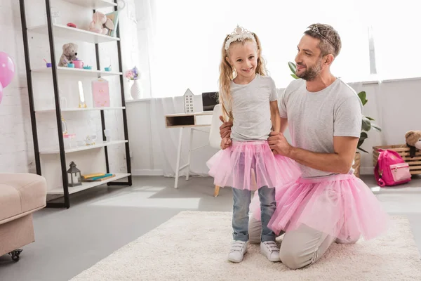 Padre e hija en faldas tutú rosadas sonriendo en casa - foto de stock