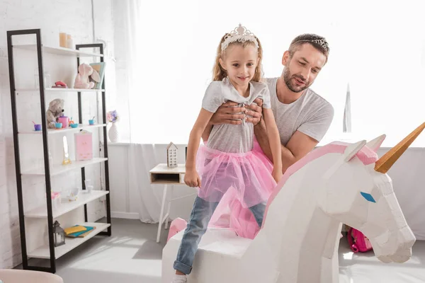 Front view of father putting daughter on unicorn — Stock Photo