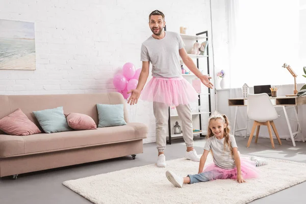 Father and daughter in pink tutu skirts, kid sitting on string at home — Stock Photo