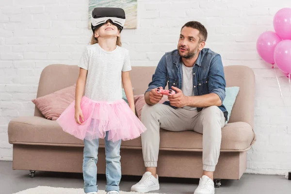 Father and daughter using virtual reality headset and joystick at home — Stock Photo