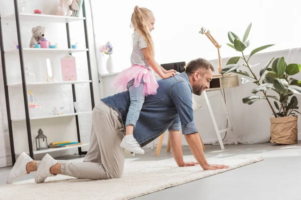 Fille assise sur le dos du père et souriant à la maison — Photo de stock