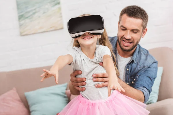 Отец и дочь веселятся и используют гарнитуру виртуальной реальности на диване — стоковое фото