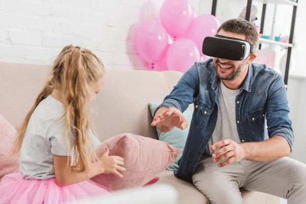 Alegre papá y su hija divertirse y el uso de auriculares de realidad virtual en el sofá - foto de stock