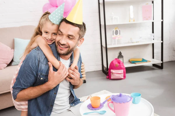 Padre e hija en sombreros de cono jugando fiesta de té en casa - foto de stock