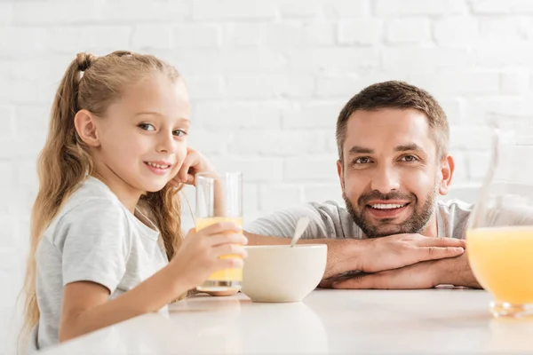 Pai e filha bebendo suco de laranja e olhando para a câmera — Fotografia de Stock