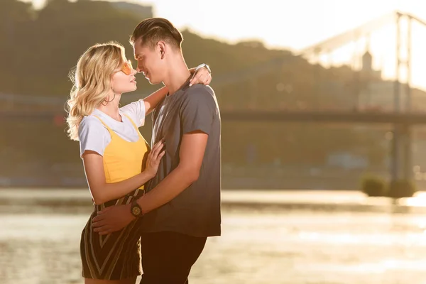 Vista laterale della giovane coppia che si abbraccia e si bacia sulla spiaggia del fiume in serata — Foto stock