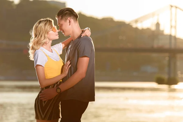 Side view of young couple hugging and going to kiss on river beach in evening — Stock Photo