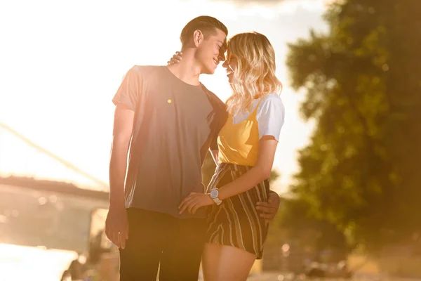 Pareja joven abrazándose y yendo a besarse en la playa del río durante el atardecer - foto de stock