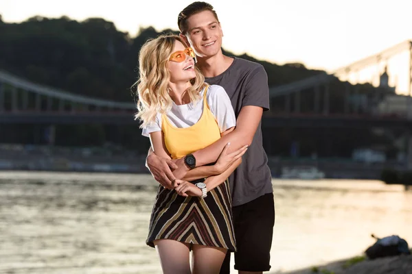 Sorridente fidanzato abbracciare fidanzata sulla spiaggia del fiume in serata — Foto stock