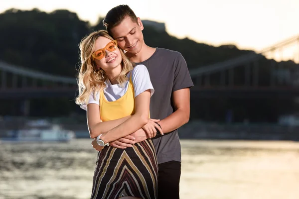Happy boyfriend hugging girlfriend on river beach in evening — Stock Photo