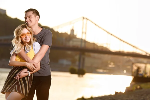 Freund umarmt Freundin am Flussstrand bei Sonnenuntergang — Stockfoto