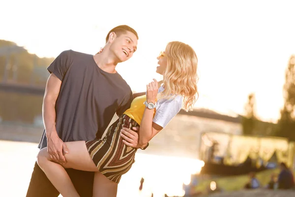 Young smiling couple hugging on river beach in evening and looking at each other — Stock Photo