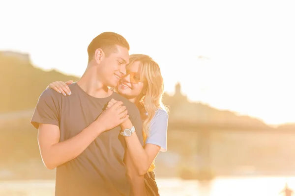 Happy girlfriend hugging boyfriend on river beach in evening — Stock Photo