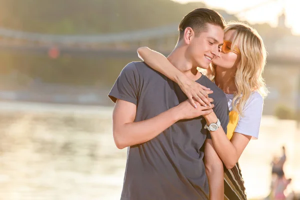 Girlfriend hugging and kissing boyfriend on river beach in evening — Stock Photo