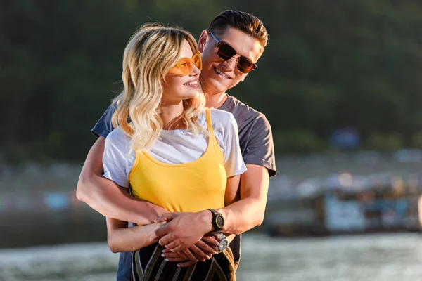 Fidanzato sorridente coccole fidanzata sulla spiaggia del fiume in serata — Foto stock