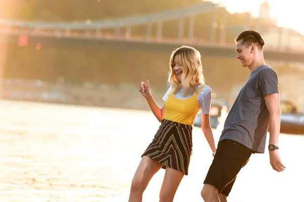 Pareja joven divirtiéndose y mirando hacia abajo en la playa del río por la noche - foto de stock