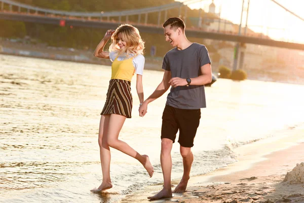 Jeune couple se tenant la main et s'amusant sur la plage de la rivière en soirée — Photo de stock
