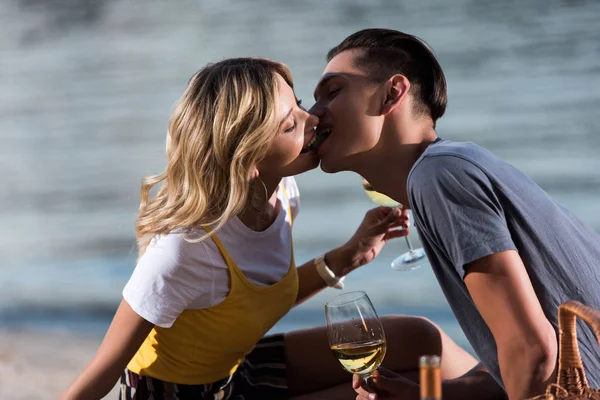 Vista lateral de pareja joven besándose en el picnic en la playa del río por la noche - foto de stock