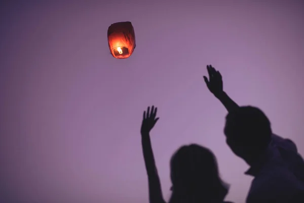 Silhouettes of couple waving hands to flying sky lantern in evening — Stock Photo