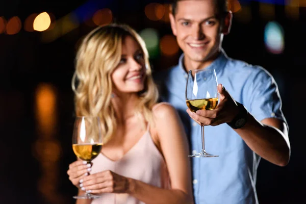 Selektiver Fokus des jungen Paares, das am Abend ein Glas Wein am Flussstrand hält — Stockfoto
