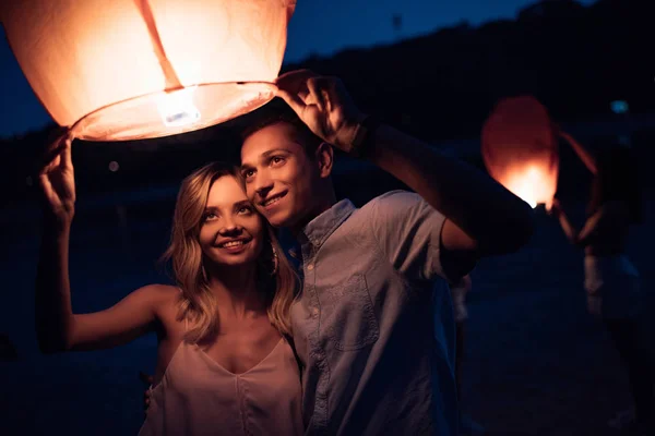 Joven pareja lanzando cielo linterna en la playa del río por la noche - foto de stock