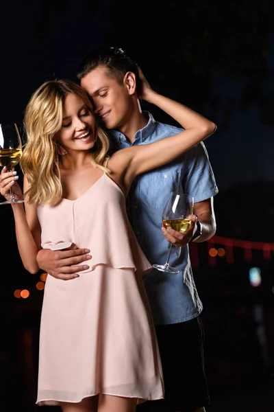 Junges Paar umarmt und hält abends am Flussstrand ein Glas Wein in der Hand — Stockfoto
