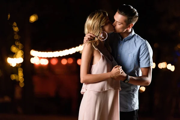 Junges Paar hält Händchen und küsst sich abends am Flussstrand — Stockfoto