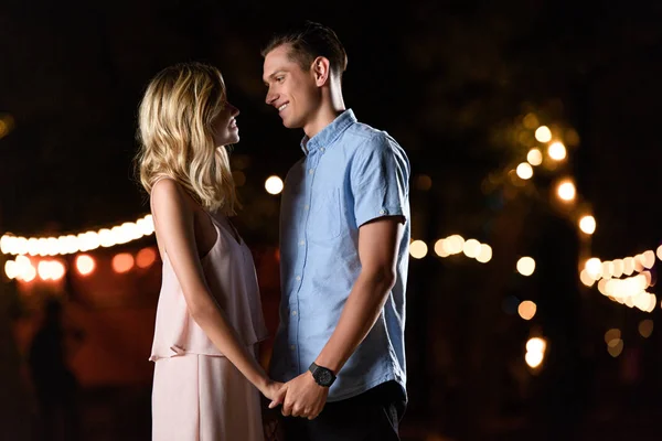 Young couple holding hands and looking at each other on river beach in evening — Stock Photo