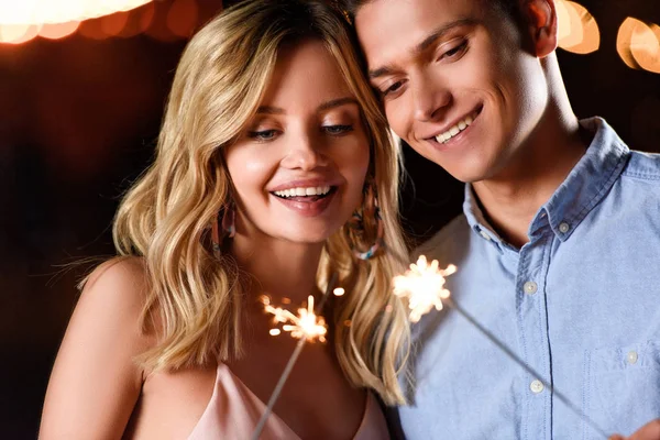 Heureux jeune couple regardant la fête scintille sur la plage de la rivière dans la soirée — Photo de stock