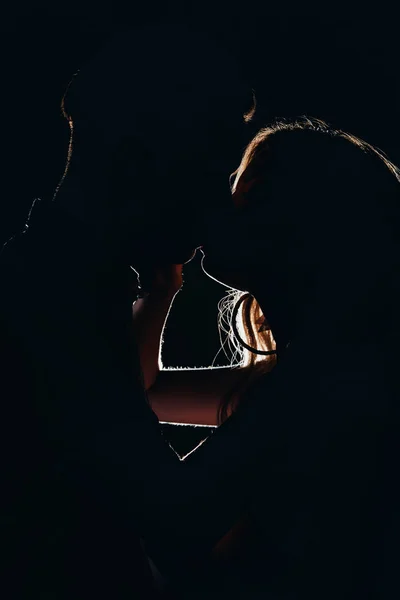Силуэты гетеросексуальной пары, целующейся в темноте — стоковое фото