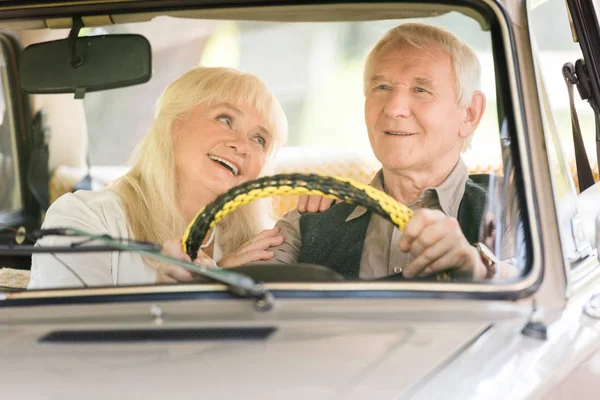 Sorrindo esposa sênior olhando para o marido dirigindo carro retro — Fotografia de Stock