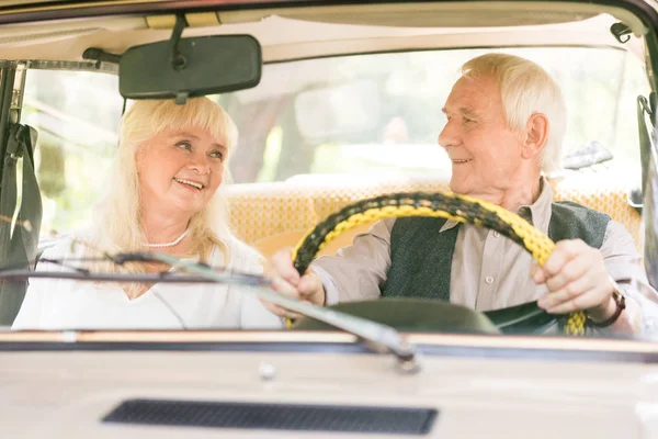 Старша пара посміхається і дивиться один на одного в старовинній машині — стокове фото