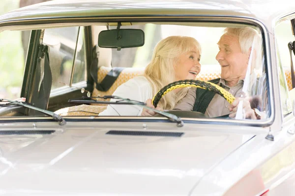 Старший чоловік і жінка посміхаються і керують старовинним автомобілем — стокове фото
