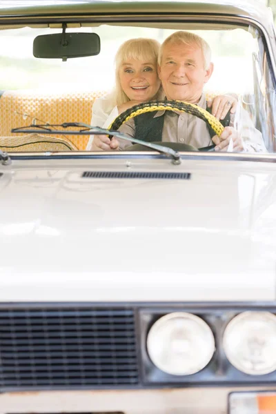 Heureux senior femme étreignant mari alors qu'il conduit voiture vintage — Photo de stock