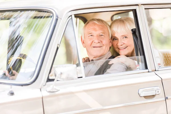 Attractive senior woman hugging man in vintage car — Stock Photo