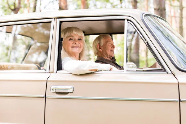 Vista lateral de la sonriente pareja mayor en coche beige - foto de stock